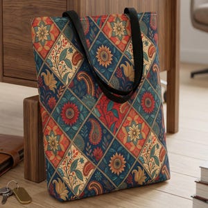 May include: A tote bag featuring a diamond-patterned print with alternating squares of sunflowers, paisley motifs, and floral vines in shades of deep blue, burnt orange, red, and cream. The bag includes two black fabric shoulder straps.