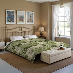 Op de afbeelding: Een groene patchwork sprei met diverse tinten groen en witte patronen, waaronder bloemen-, ruit- en geometrische ontwerpen, gedrapeerd over een bed met een messing hoofdeinde en een crèmekleurige gecapitonneerde opbergbank aan het voeteneinde.