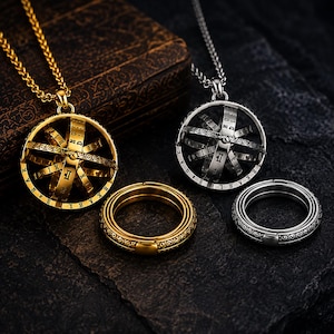 Puede incluir: Un collar con colgante de esfera armilar en tono dorado y otro en tono plateado, cada uno con un anillo a juego. Los colgantes esféricos tienen bandas giratorias grabadas con números romanos y letras, suspendidos de cadenas de trigo.