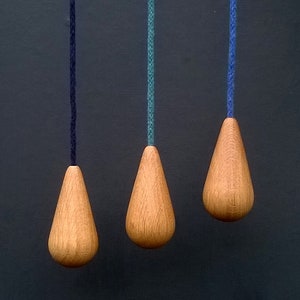 May include: Three wooden light pull chains with different coloured cords. The cords are black, teal and blue. The wooden pulls are teardrop shaped.
