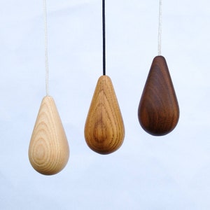 May include: Three wooden light pull pendants in different wood tones. The pendants are shaped like teardrops and are hanging from cords.