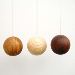 May include: Three wooden balls hanging from white cords. The balls are different shades of brown, with one being a light brown, one a medium brown, and one a dark brown.