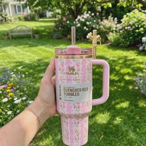 May include: A pink floral Stanley Quencher H2.0 Tumbler with a handle and straw. The tumbler has a pink lid and handle, and a floral pattern in shades of pink and purple. The text on the label reads "Stanley Quencher H2.0 Tumbler".