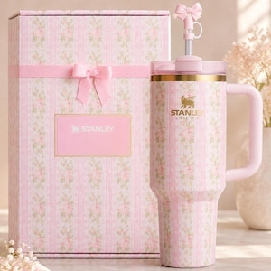 Peut inclure: Un gobelet Stanley rose &agrave; motifs floraux avec une poign&eacute;e et une bo&icirc;te cadeau assortie. Le gobelet a un bord dor&eacute; et un dessus en forme de n&oelig;ud. La bo&icirc;te cadeau est d&eacute;cor&eacute;e d'un ruban et d'un n&oelig;ud roses et porte le logo Stanley.