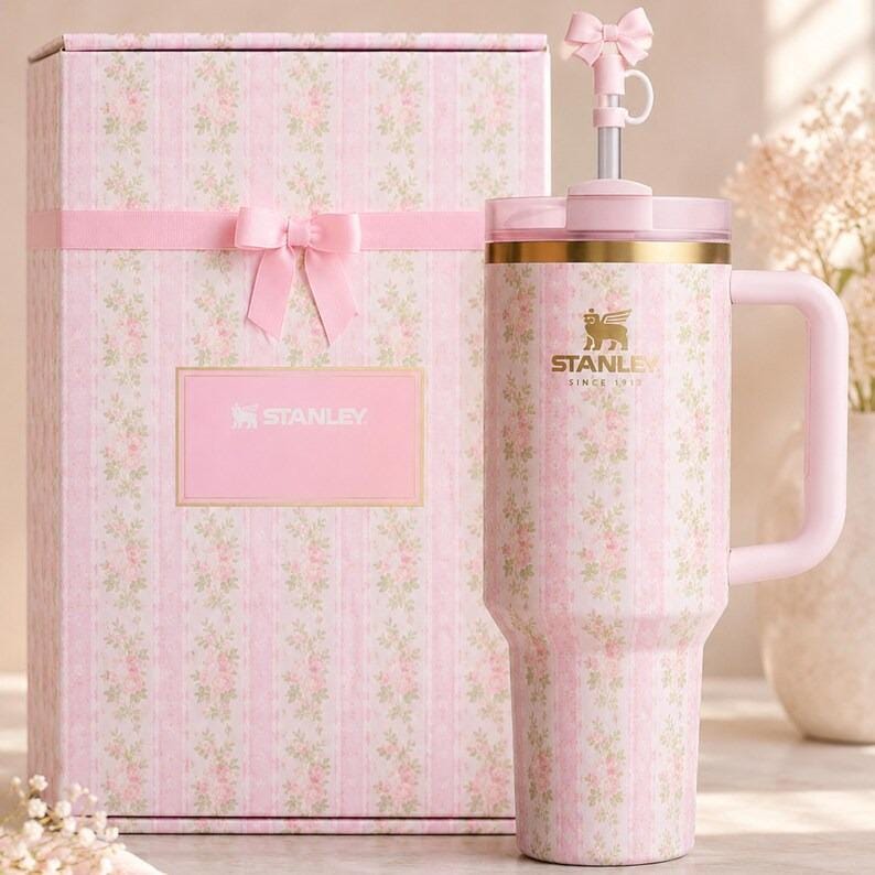 Peut inclure: Un gobelet Stanley rose &agrave; motifs floraux avec une poign&eacute;e et une bo&icirc;te cadeau assortie. Le gobelet a un bord dor&eacute; et un dessus en forme de n&oelig;ud. La bo&icirc;te cadeau est d&eacute;cor&eacute;e d'un ruban et d'un n&oelig;ud roses et porte le logo Stanley.