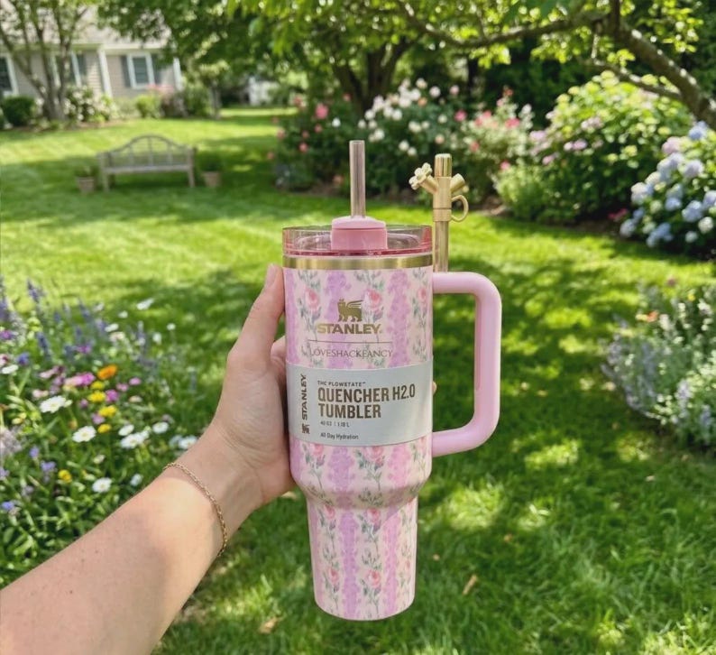 May include: A pink floral Stanley Quencher H2.0 Tumbler with a handle and straw. The tumbler has a pink lid and handle, and a floral pattern in shades of pink and purple. The text on the label reads "Stanley Quencher H2.0 Tumbler".
