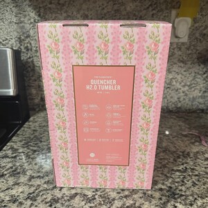May include: A pink box with a floral pattern and the text "QUENCHER H2.0 TUMBLER". The box has a rectangular label with product information and icons. The tumbler holds 40 oz, or 1.18 L.