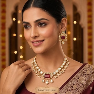 May include: A gold-toned necklace and matching earrings set featuring rectangular red stones, clear white stones, and small white pearl-like beads. The necklace has a central red stone pendant with dangling accents. The text LakeFront Glams is visible.