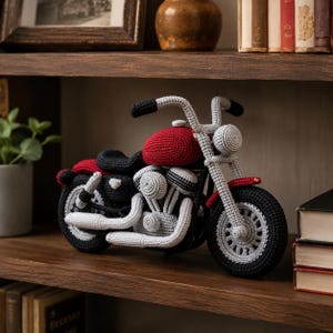 May include: A handmade crochet motorcycle in red, black, and gray. The toy motorcycle features a red fuel tank, black seat, and gray engine components. The wheels are black with gray detailing. The motorcycle is displayed on a wooden shelf.