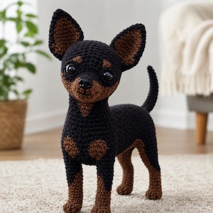 Può includere: Figurina di cane all'uncinetto, prevalentemente nera con dettagli marroni su orecchie, muso e zampe. Il cane ha grandi occhi e una coda arricciata. La statuetta è posizionata su un tappeto dai toni neutri, mettendo in risalto l'artigianato.