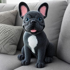 Può includere: Un cane bulldog francese all'uncinetto grigio scuro, fatto a mano, con un marchio bianco sul petto, orecchie interne rosa e occhi blu. Il cane è seduto su un divano grigio, mostrando la sua dettagliata maestria artigianale e il suo design giocoso. Un oggetto decorativo affascinante.