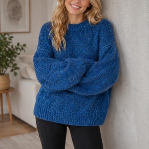 Puede incluir: Un suéter de punto grueso de manga larga en un vibrante color azul real con sutiles motas multicolores en toda la tela. El suéter presenta un cuello redondo clásico, puños acanalados y un dobladillo acanalado, combinado con leggings negros lisos.