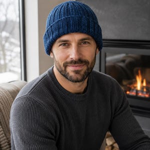 May include: A deep blue knit beanie with a thick ribbed texture and a folded cuff. The hat is constructed from a dark, multi-tonal blue yarn, featuring a vertical ribbed pattern that runs from the crown down to the wide, folded brim edge.