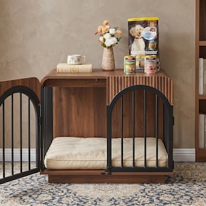 May include: A wooden dog crate with a dark walnut finish, featuring two arched black metal doors and a cream-colored rectangular cushion inside. The top surface holds a beige vase with flowers, a book, and two cans of dog food next to a bag.