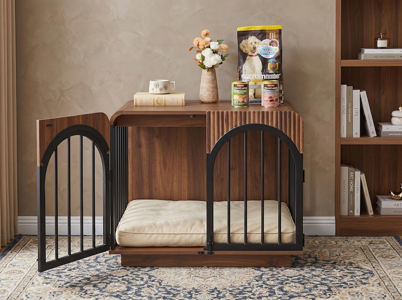 May include: A wooden dog crate with a dark walnut finish, featuring two arched black metal doors and a cream-colored rectangular cushion inside. The top surface holds a beige vase with flowers, a book, and two cans of dog food next to a bag.