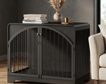 Könnte beinhalten: Eine dunkelgraue Hundebox mit gewölbter Oberseite und gewölbten Metallstäben an der Vorderseite. Die Box hat zwei Türen und ein dekoratives Design. Eine Vase mit getrockneten Blumen, Bücher und eine Tasse stehen oben.