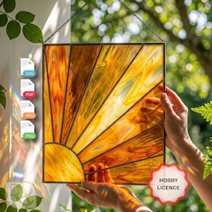 May include: A square stained glass suncatcher featuring a radiating sunburst pattern in shades of amber, gold, and orange. The glass panels are held together by dark metal cames. A black chain is attached to the top for hanging purposes.