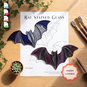 May include: A paper pattern titled Bat Stained Glass featuring two finished bat-shaped stained glass pieces, one in blue and one in purple, placed over a numbered outline. The document includes file format icons, a hobby licence badge, and text.