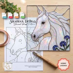 May include: A stained glass panel of an Arabian horse with iridescent white glass and blue flower accents, displayed alongside a printed paper pattern, a glass cutter tool, and a roll of copper foil tape for crafting projects.