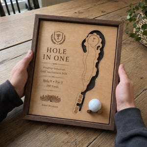Peut inclure: Une plaque murale encadrée en bois avec une carte de terrain de golf gravée au laser, une balle de golf blanche et le texte HOLE IN ONE, Foxdrop Industries Golf Tournament 2026, Hole 9, Par 3, 168 Yards, et Royal Bromont avec une icône de trophée.