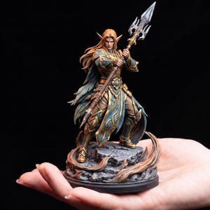 Peut inclure: Une figurine détaillée d'un guerrier elfe aux cheveux longs et aux oreilles pointues, portant une armure ornée bleu sarcelle et dorée. La figurine se tient sur une base rocheuse, tenant une longue lance argentée avec une pointe acérée.