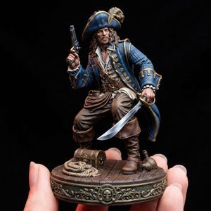 Op de afbeelding: Gedetailleerd beeldje van een piraat in een blauwe jas en hoed, met een pistool en een sabel. De piraat staat op een houten voet met een schatkist en touw, met een doodshoofd ontwerp. Het beeldje is ongeveer 15 cm hoog.