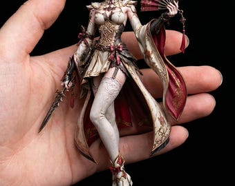 May include: A detailed figurine of a female character in an ornate outfit, holding a fan and a sword. The figure has white hair and is dressed in a cream, gold, and burgundy ensemble. The figurine is on a black base.