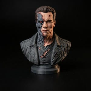 May include: A detailed bust of a human figure with a damaged face revealing mechanical components and a glowing red eye. The figure wears a distressed dark gray jacket with visible tears and rips, set against a solid black background.