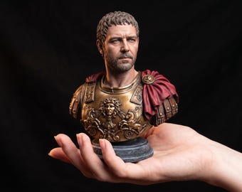 May include: A detailed bust of a man with short brown hair and a beard, wearing bronze-colored armor with a central Gorgon emblem and a draped red cloak over the left shoulder, set upon a circular dark gray base against a black background.