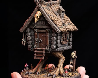 May include: A miniature wooden cabin with a thatched roof, perched on two large bird-like legs. The structure features a central door, a small window, a skull mounted above the entrance, and a small post with a skull nearby, all on a round base.