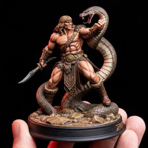 May include: A detailed figurine of a muscular warrior with long blonde hair, clad in fur and leather armour, holding a sword and facing a large snake. The snake is coiled around the warrior, its head raised in a striking pose. The base is dark with a rocky texture.