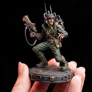 Puede incluir: Figura en miniatura de un soldado en posición de combate, sosteniendo un arma futurista. La figura viste uniforme verde oliva, casco y mochila. La base es una plataforma circular con diseño de calavera. La figura mide unos 10 cm de altura.