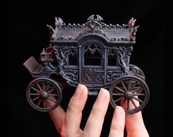 May include: A miniature dark gray carriage model featuring intricate scrollwork, arched windows, and bat-shaped finials on the roof. The carriage has four spoked wheels and a driver's seat, with detailed relief patterns covering the exterior walls.