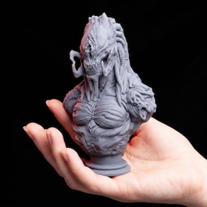 May include: A gray, unpainted resin bust of a creature with a textured, alien-like head featuring mandibles, dreadlock-style appendages, and a muscular torso. The sculpture is detailed with intricate ridges and organic patterns throughout.