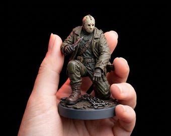May include: A detailed figurine of Jason Voorhees, the iconic horror movie character, kneeling and holding a knife. The figure wears a hockey mask, a brown jacket, and olive green pants. The base is gray with a chain.