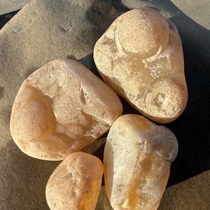 Puede incluir: Cuatro piedras translúcidas de color naranja claro y beige con superficies lisas y redondeadas y formas orgánicas irregulares. Las piedras presentan una textura semicristalina con patrones internos visibles y diversos grados de opacidad.
