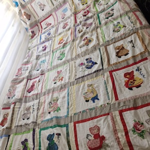 Puede incluir: Una colcha blanca con una cuadrícula de cuadrados bordados, cada uno mostrando una figura única con ropa colorida. Los cuadrados están separados por tiras de tela de varios colores, incluyendo rojo, verde, azul y amarillo, creando un diseño de patchwork.