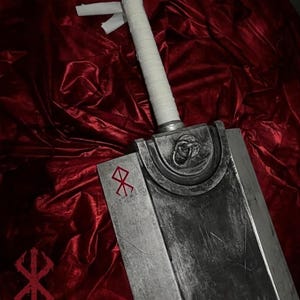 May include: A large, heavy-looking sword with a weathered, metallic silver finish and a white-wrapped handle. The blade features a prominent circular metal detail near the hilt and a distinct red runic symbol etched onto the flat surface.