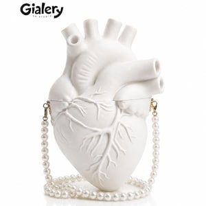 Puede incluir: Un bolso de mano blanco con forma de corazón anatómico y acabado mate, que presenta vasos sanguíneos y cámaras moldeadas. El bolso incluye una correa de hombro desmontable hecha de perlas blancas con cierres de metal dorado. El logotipo de Gialery 3D Studio es visible.