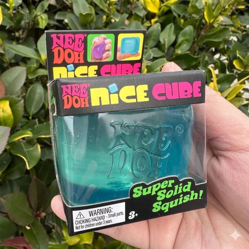May include: A Nee Doh Nice Cube toy in a clear plastic container. The cube is a translucent teal colour. The packaging has the words "Nee Doh" and "Nice Cube" in colourful text. The package also says "Super Solid Squish!"