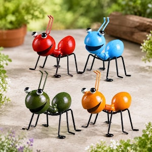 May include: Four metal ant figurines in red, blue, green, and orange. Each ant features a rounded head with two antennae, large white eyes with black pupils, a wide smiling mouth, a segmented body, and six thin black wire legs for support.