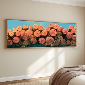 May include: A panoramic wall art print featuring a stacked pile of circular cut logs with reddish-orange wood grain centers and light brown bark edges, set against a bright blue sky background, all enclosed within a thin, light-colored wooden frame.