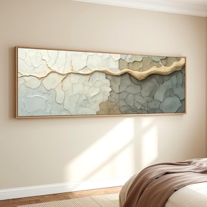 May include: Abstract wall art in a rectangular wooden frame. The artwork features a textured surface with a cracked, layered design in shades of white, grey, and beige. A raised, golden-brown element runs horizontally across the centre.