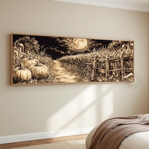 May include: A panoramic wall art print in a light wood frame featuring a sepia-toned illustration of a moonlit cornfield at night. The scene depicts two large pumpkins in the foreground, a dirt path leading into the field, and a wooden fence.
