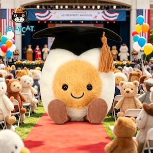 May include: A plush, egg-shaped toy wearing a black graduation cap with a gold tassel. The egg has a yellow yolk, white egg whites, and corduroy feet. The background shows a graduation ceremony with teddy bears.