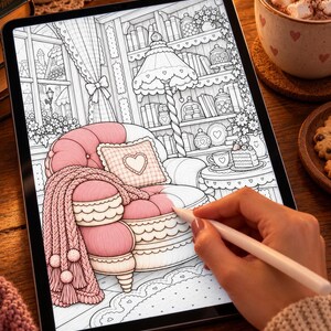 May include: A digital tablet displaying a black and white line art colouring page of a cosy room interior featuring a plush armchair with a heart-patterned pillow and a knitted throw blanket, partially coloured in shades of soft pink.