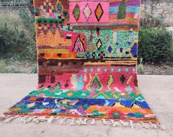May include: A rectangular hand-knotted wool rug featuring a vibrant, multi-colored geometric pattern. The design includes various shapes like diamonds and triangles in shades of hot pink, orange, green, blue, and brown, finished with white fringe.