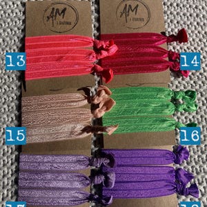 May include: Six sets of colorful hair ties, each set containing three ties. The colors are pink, peach, green, purple, and a darker purple. Each set is labeled with a number from 13 to 18.