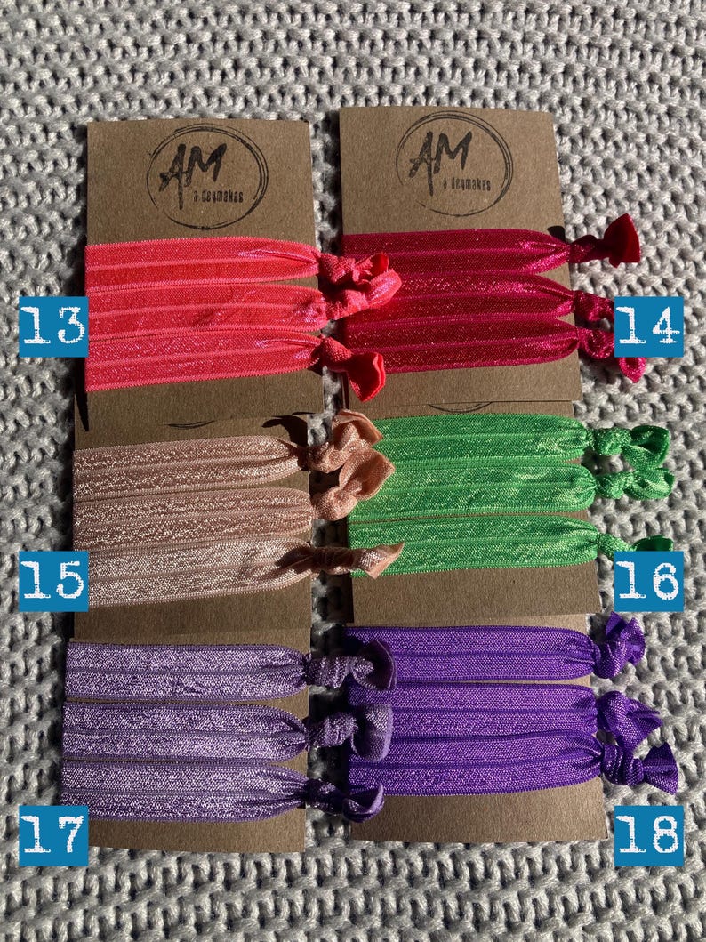 May include: Six sets of colorful hair ties, each set containing three ties. The colors are pink, peach, green, purple, and a darker purple. Each set is labeled with a number from 13 to 18.