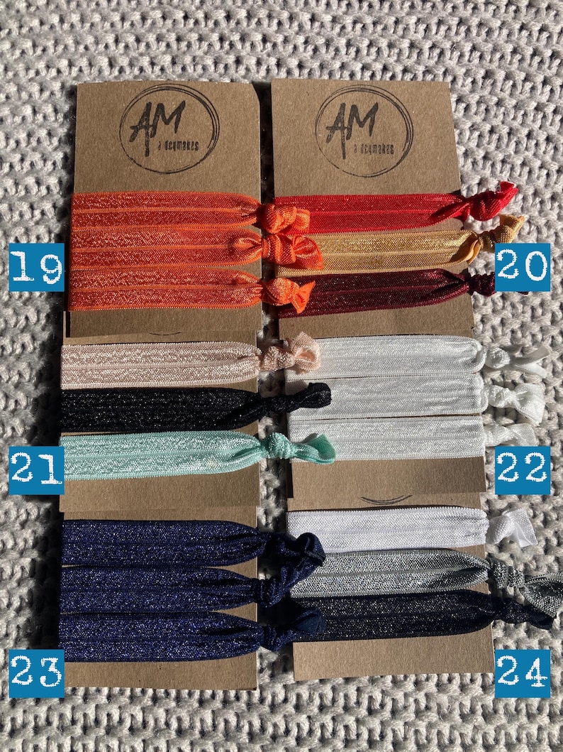 May include: Set of 10 colorful hair ties, packaged in pairs on brown cards with the text "AM Accessories". The hair ties are made of elastic and come in a variety of colors, including orange, red, gold, burgundy, beige, black, light blue, white, silver, and navy blue.